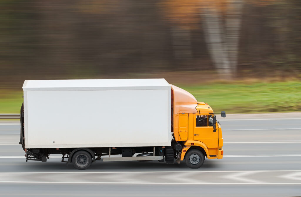 Gele vrachtwagen met witte laadruimte rijdt over de snelweg met vervaagde achtergrond die snelheid aangeeft.
